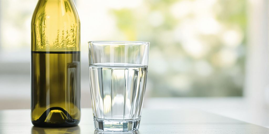 Glass of water next to an empty wine bottle.